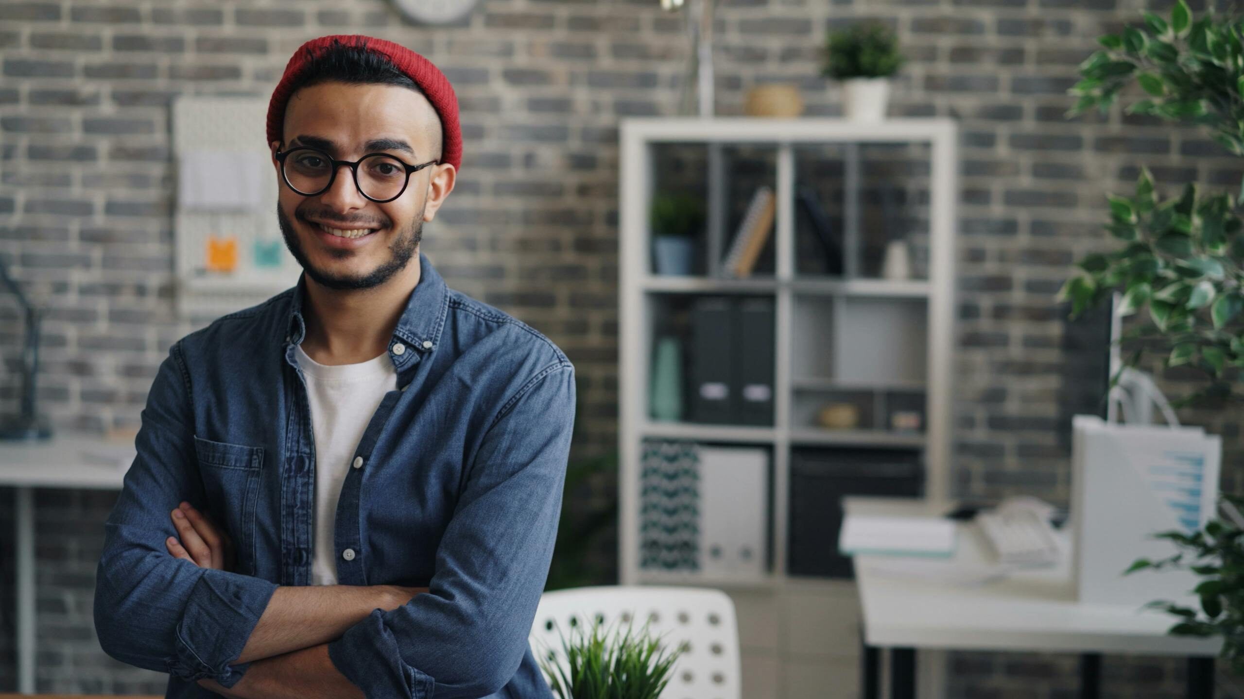 Confident young man in glasses smiling at camera in a stylish office setting.
